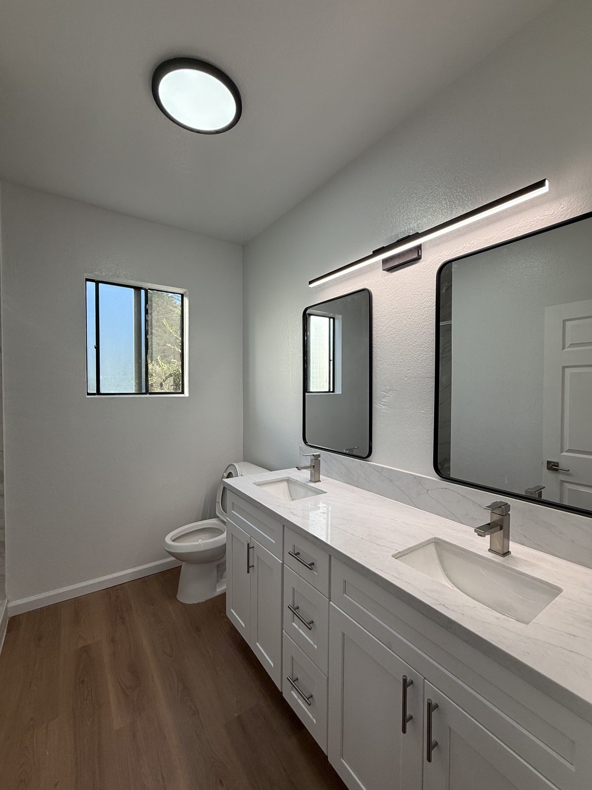 Finished bathroom with double vanity, marble countertop, and new lighting